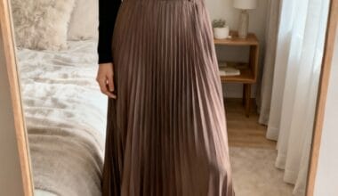 Person taking a mirror selfie wearing a black turtleneck, brown pleated midi skirt with a black belt, and pointed brown ankle boots in a bedroom.