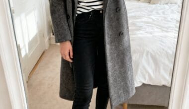 Person taking a mirror selfie wearing a gray coat, black jeans, black loafers, and a white and black striped shirt in a bedroom.